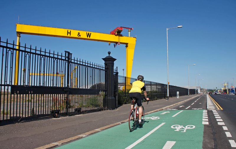 Cyclist using a cycle lane in Belfast’s Titanic Quarter with Harland and Wolff cranes in the background.